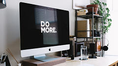 Schreibtisch mit Mac-Monitor, auf dem "DO MORE" steht